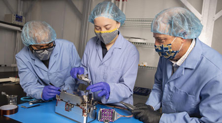 three researchers wearing masks and protective gear while working in the lab